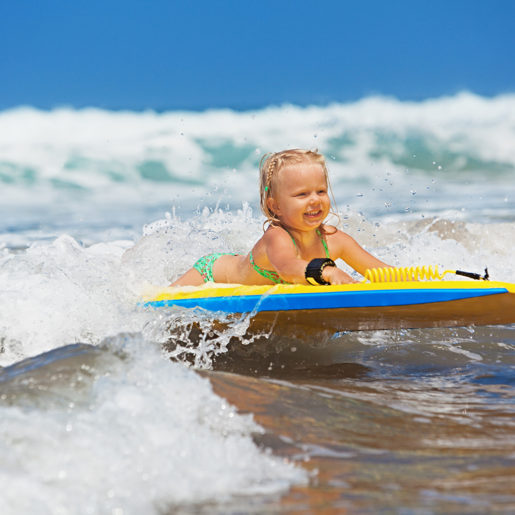 Маленькая девочка в море на доске для серфинга