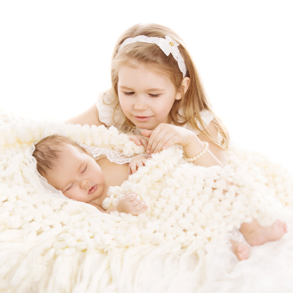 Маленькая девочка в белом со спящим младенцем на белом фоне