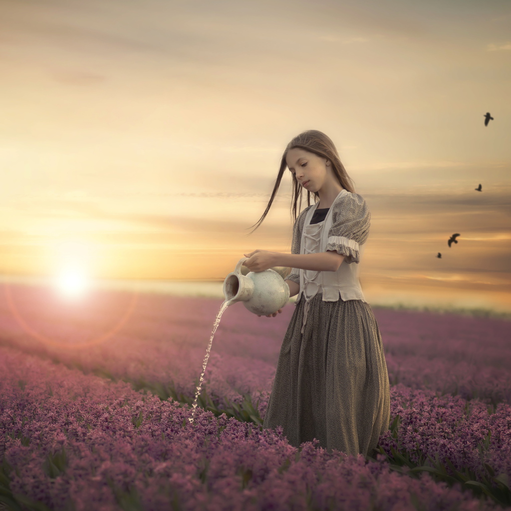 Маленькая девочка поливает цветы из кувшина в поле на закате