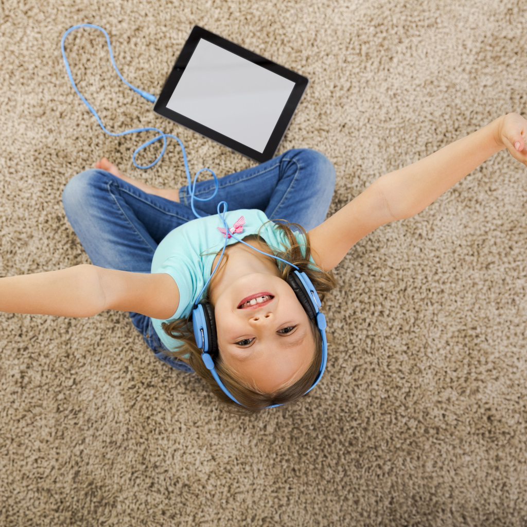Маленькая девочка слушает музыку в наушниках сидя на ковре