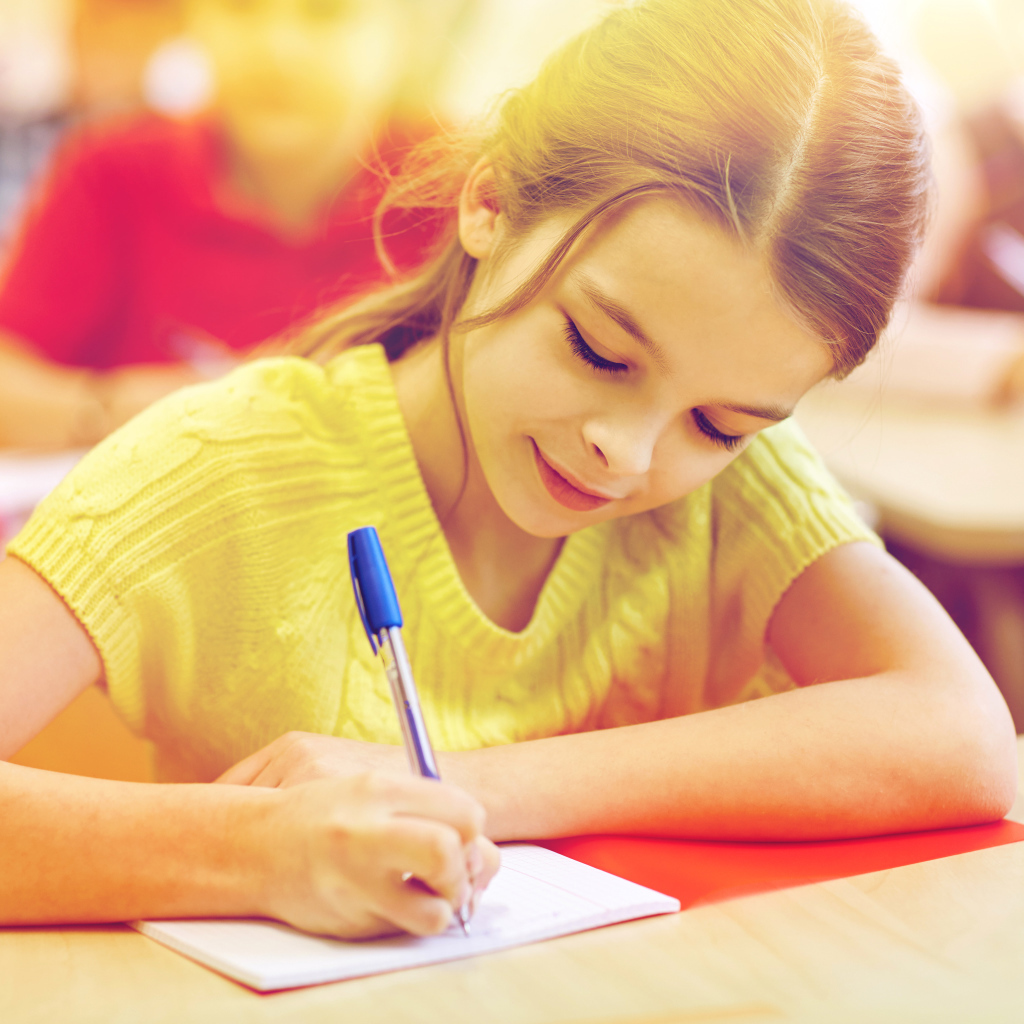 Маленькая девочка школьница пишет ручкой в тетради