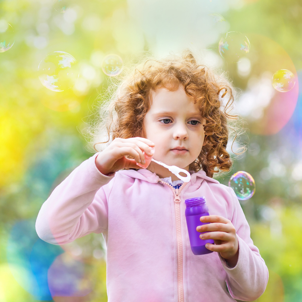 Маленькая рыжеволосая кудрявая девочка с мыльными пузырями
