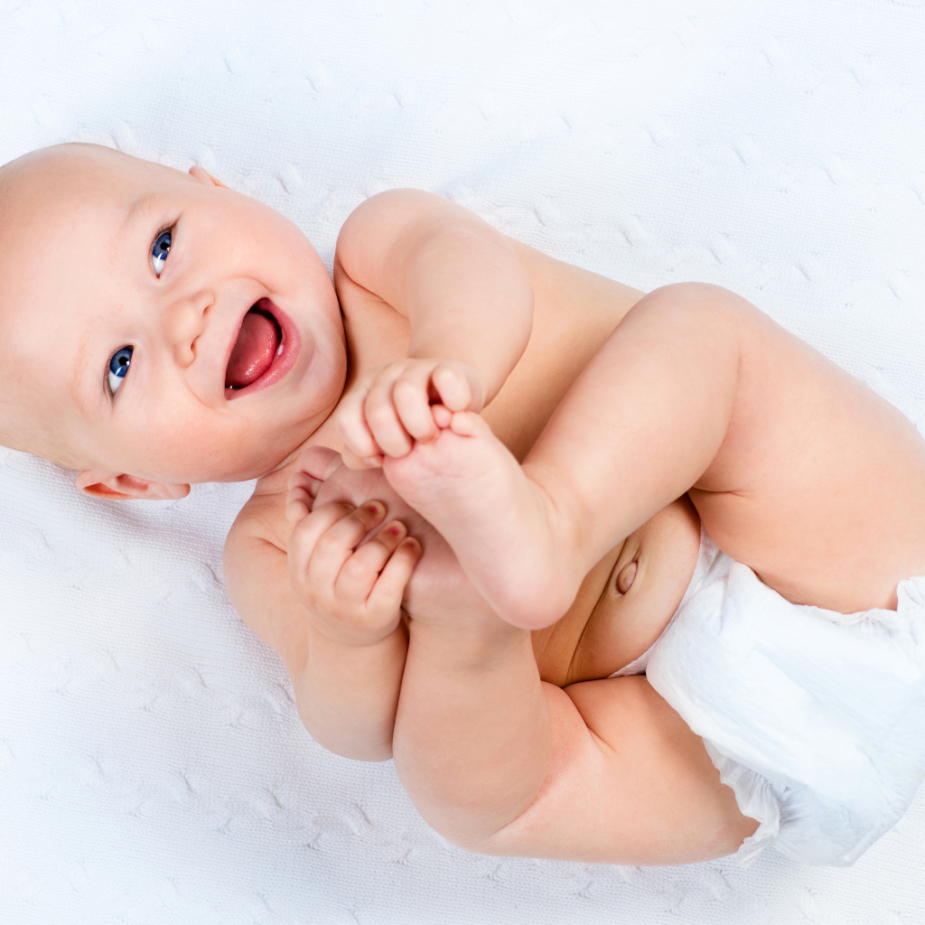 Маленький улыбающийся грудной ребенок держит руками ноги