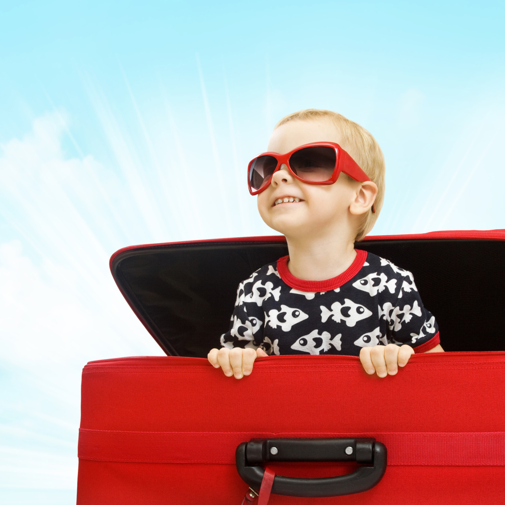 Маленький улыбающийся мальчик в очках сидит в красном чемодане