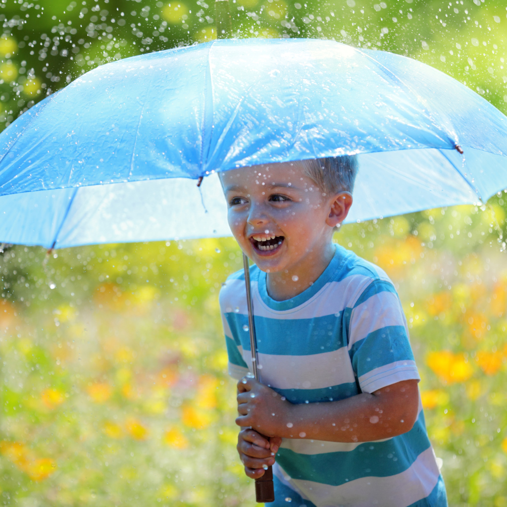 Маленький улыбающийся мальчик с голубым зонтом под дождем