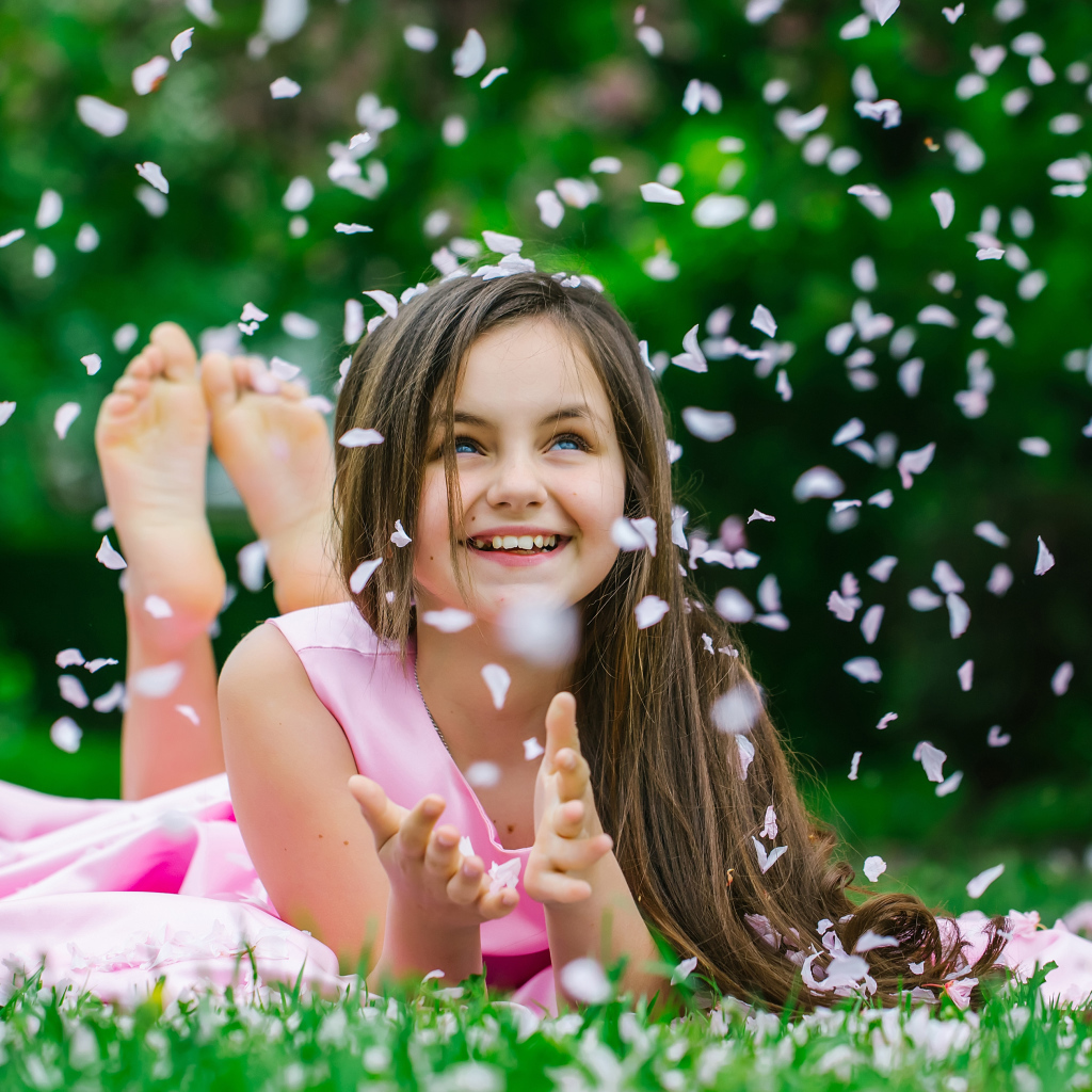 Маленькая улыбающаяся девочка шатенка ловит лепестки