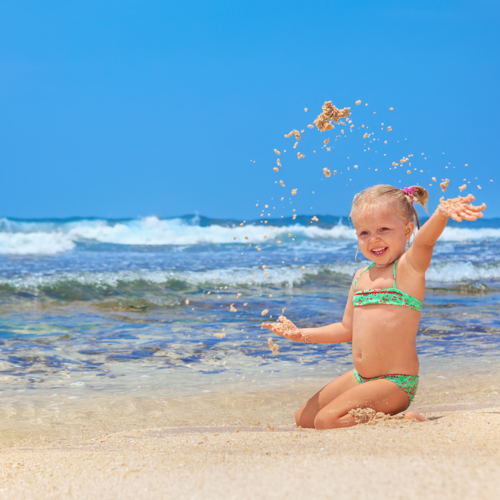 Маленькая улыбающаяся девочка играет на пляже с песком