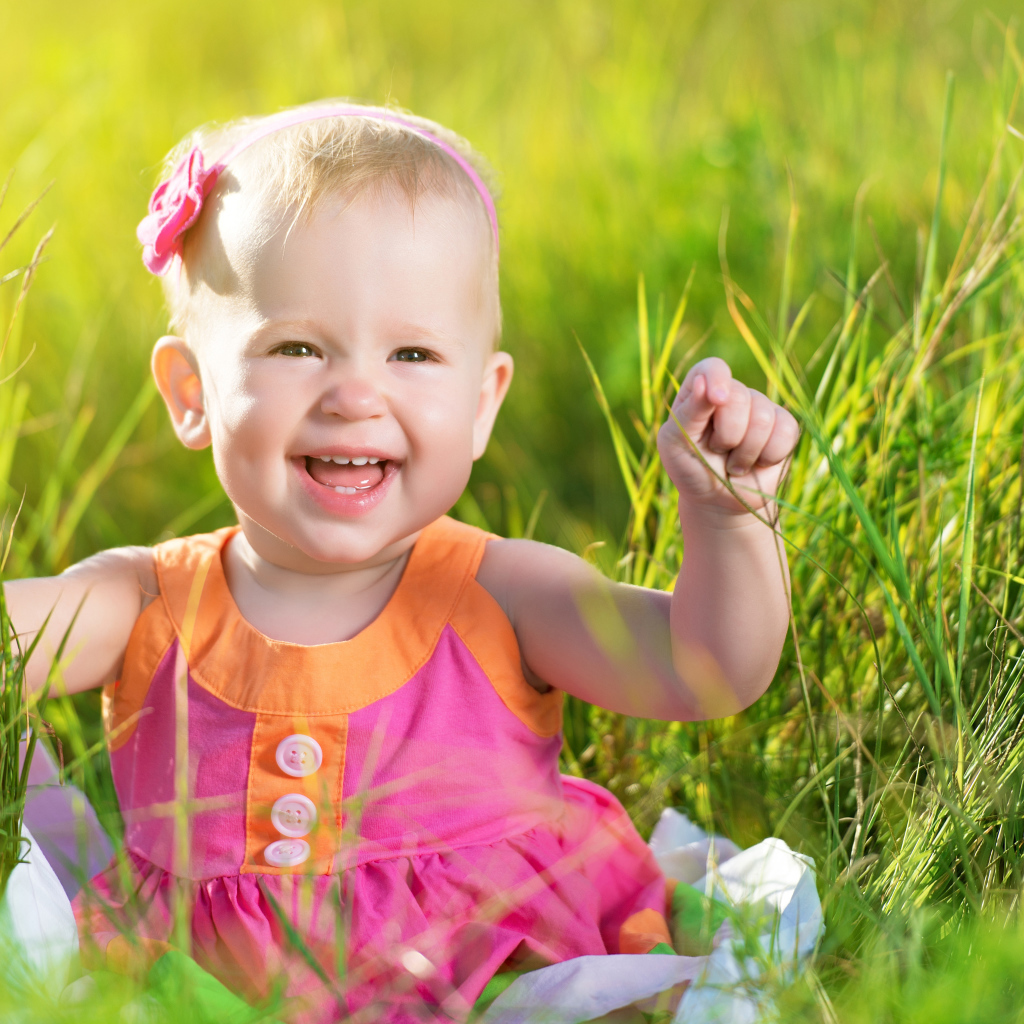 Маленькая улыбающаяся девочка сидит в зеленой траве