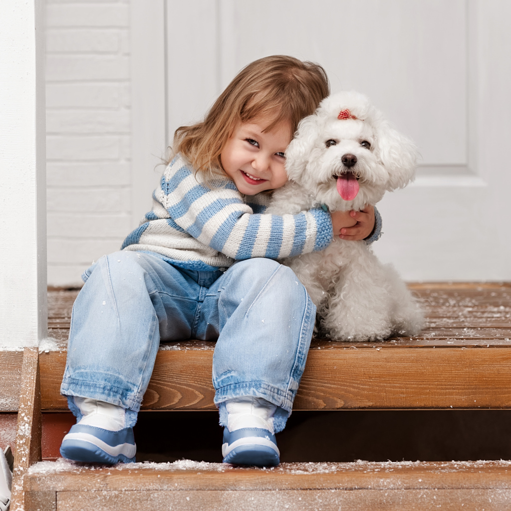 Маленькая улыбающаяся девочка сидит с белым пуделем на ступеньках