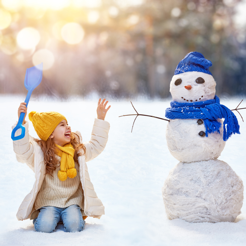 Маленькая улыбающаяся девочка со снеговиком зимой