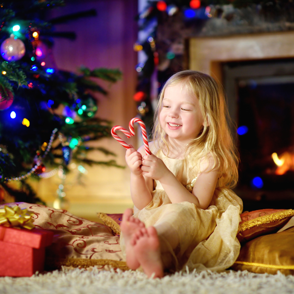 Длинноволосая девочка блондинка с леденцами у новогодней елки