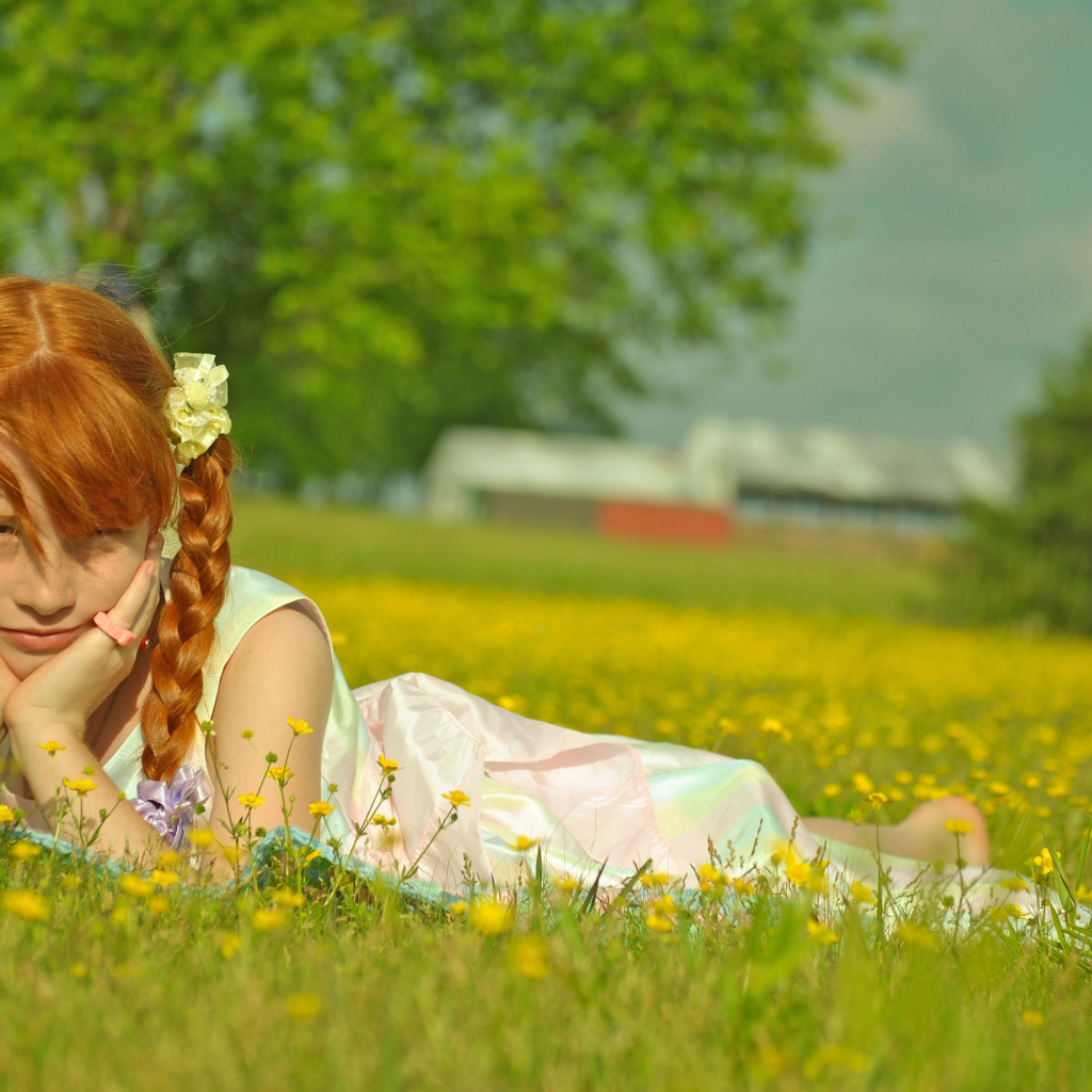 Рыжеволосая девочка с косичками лежит на зеленой траве