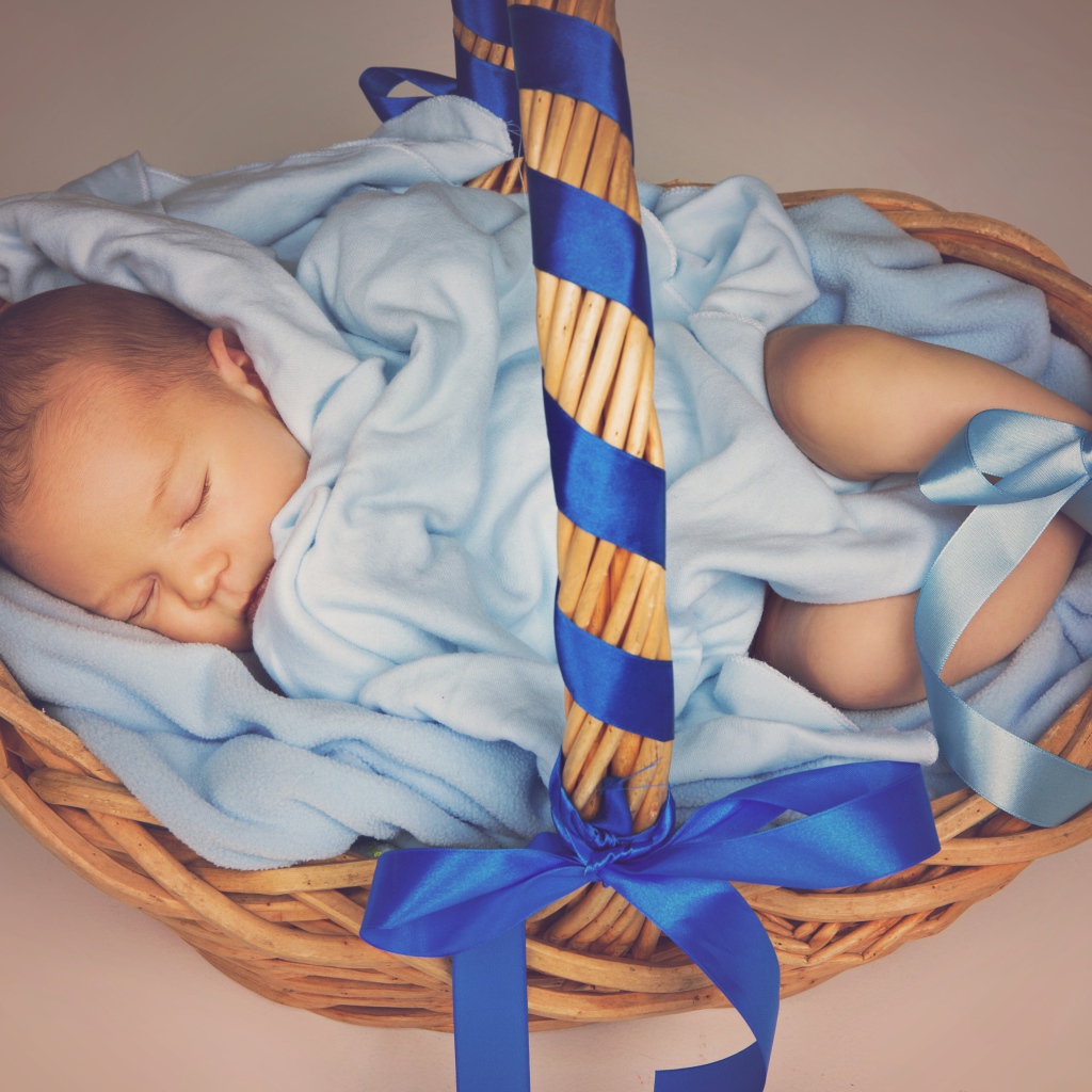 Спящий грудной ребенок в корзине с синими лентами