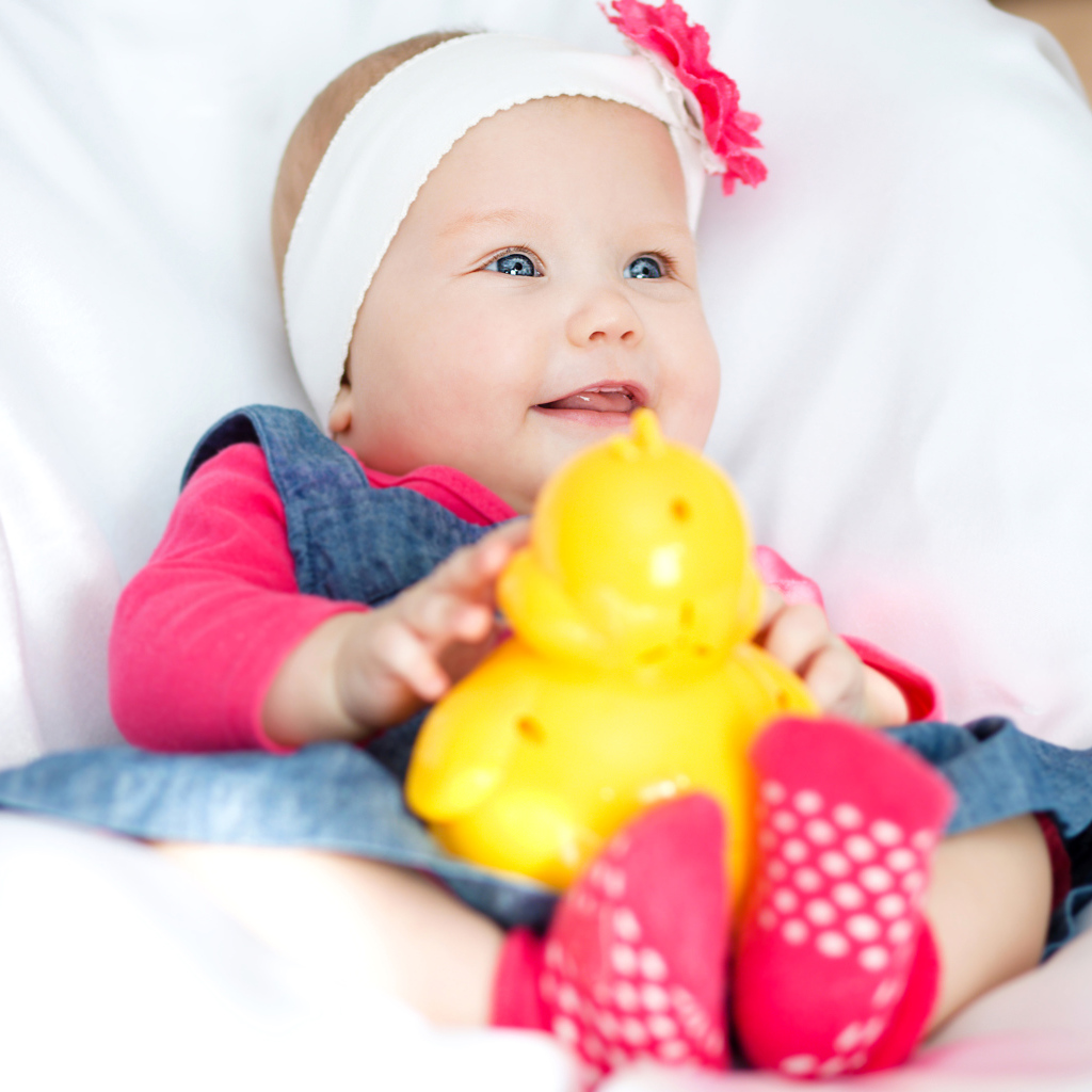 Улыбающаяся голубоглазая девочка младенец с игрушкой в руках