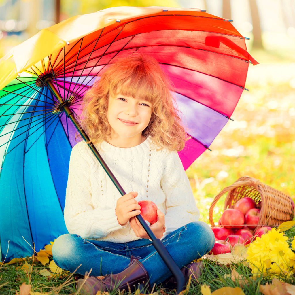 Улыбающаяся девочка под сидит под разноцветным зонтом