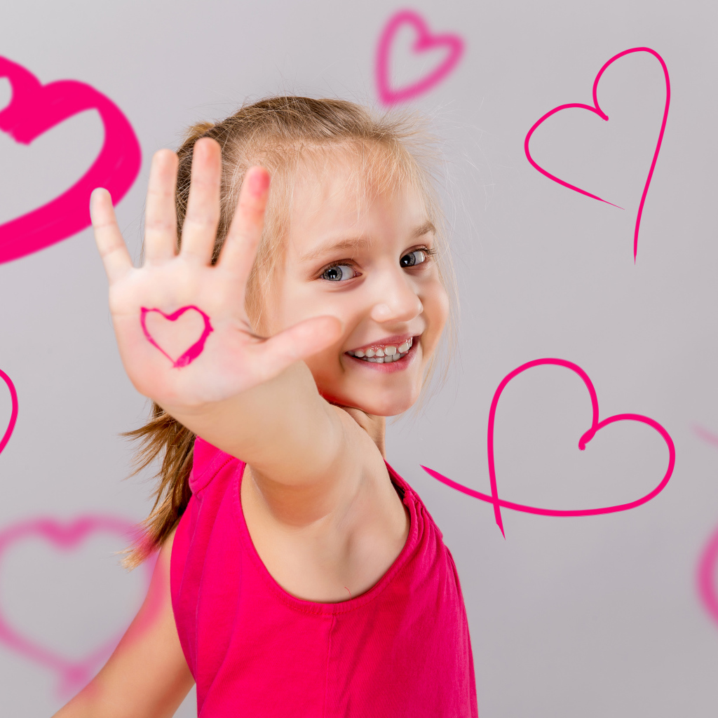 Улыбающаяся девочка с нарисованными сердечками на сером фоне