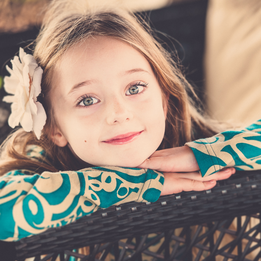 Улыбающаяся зеленоглазая девочка с белым цветком в волосах