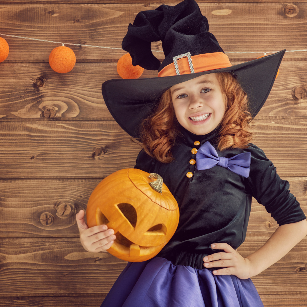 Улыбающаяся маленькая девочка в костюме ведьмы с тыквой на Хэллоуин