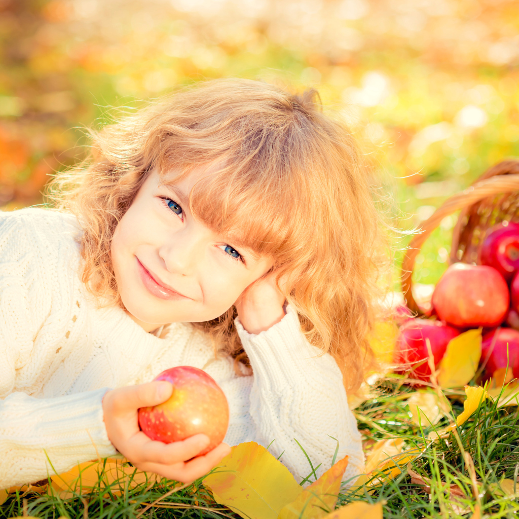 Улыбающаяся рыжеволосая девочка с корзиной красных яблок