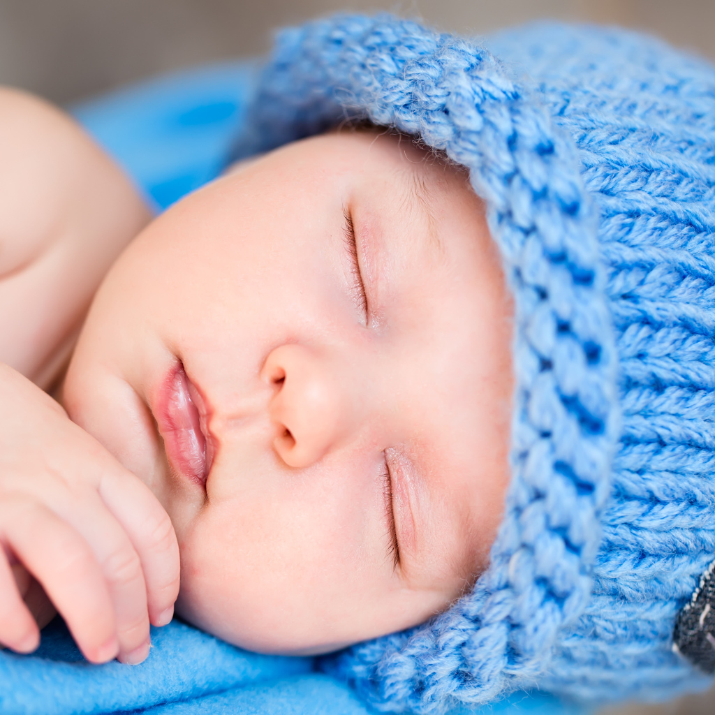 Милый спящий младенец с синей вязаной шапке