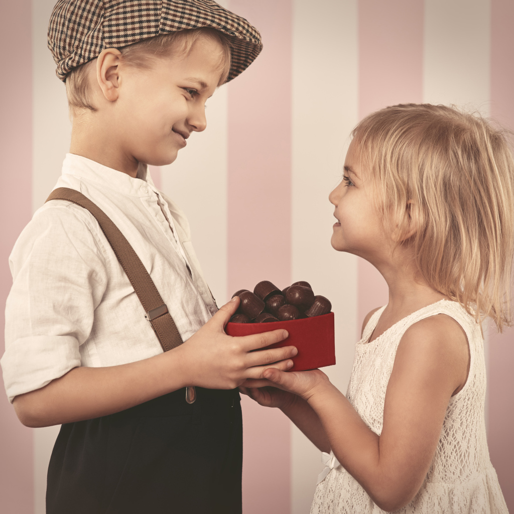 Мальчик дарит девочке коробку шоколадных конфет