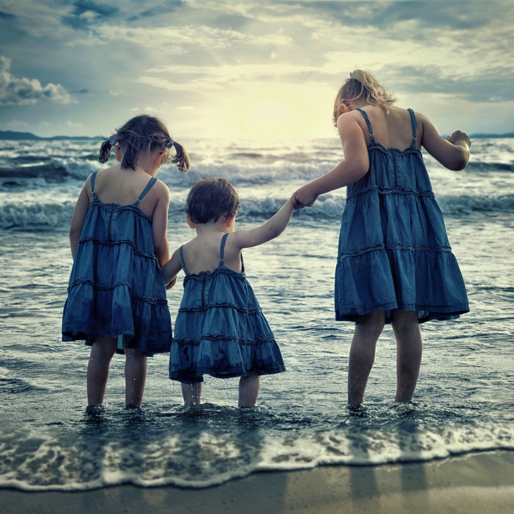 Три маленькие девочки стоят в воде на берегу моря