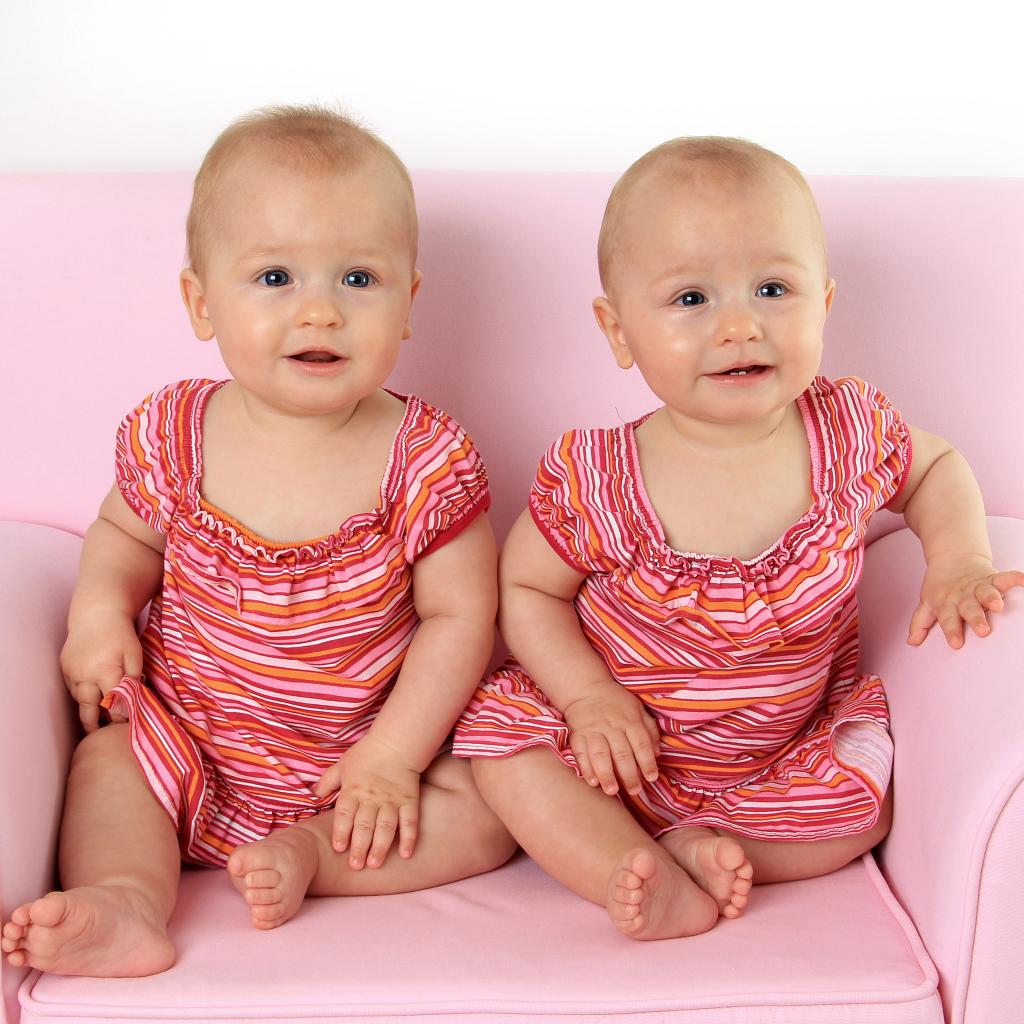 Две милые маленькие девочки сидят на розовом диване