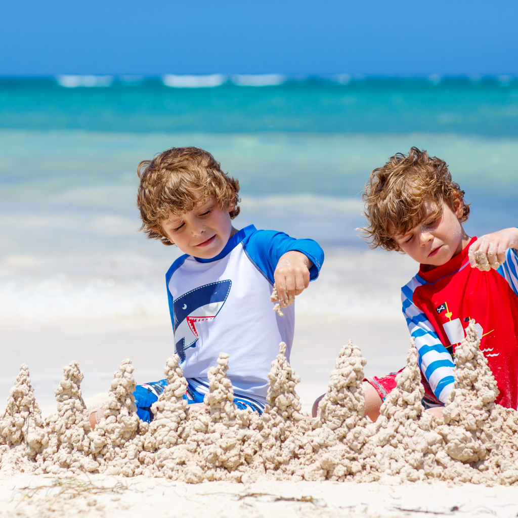 Два маленьких мальчика играют с песком на пляже