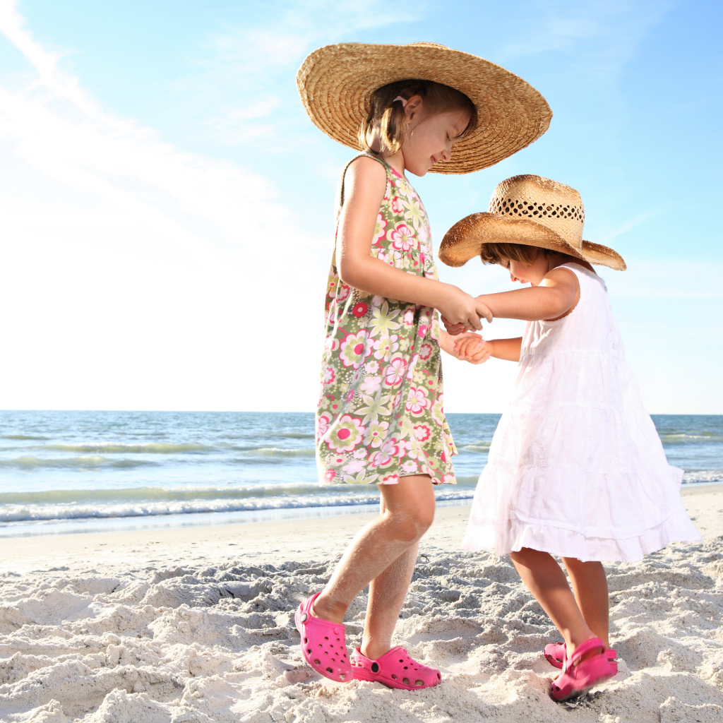 Две маленькие девочки танцуют на песке на пляже