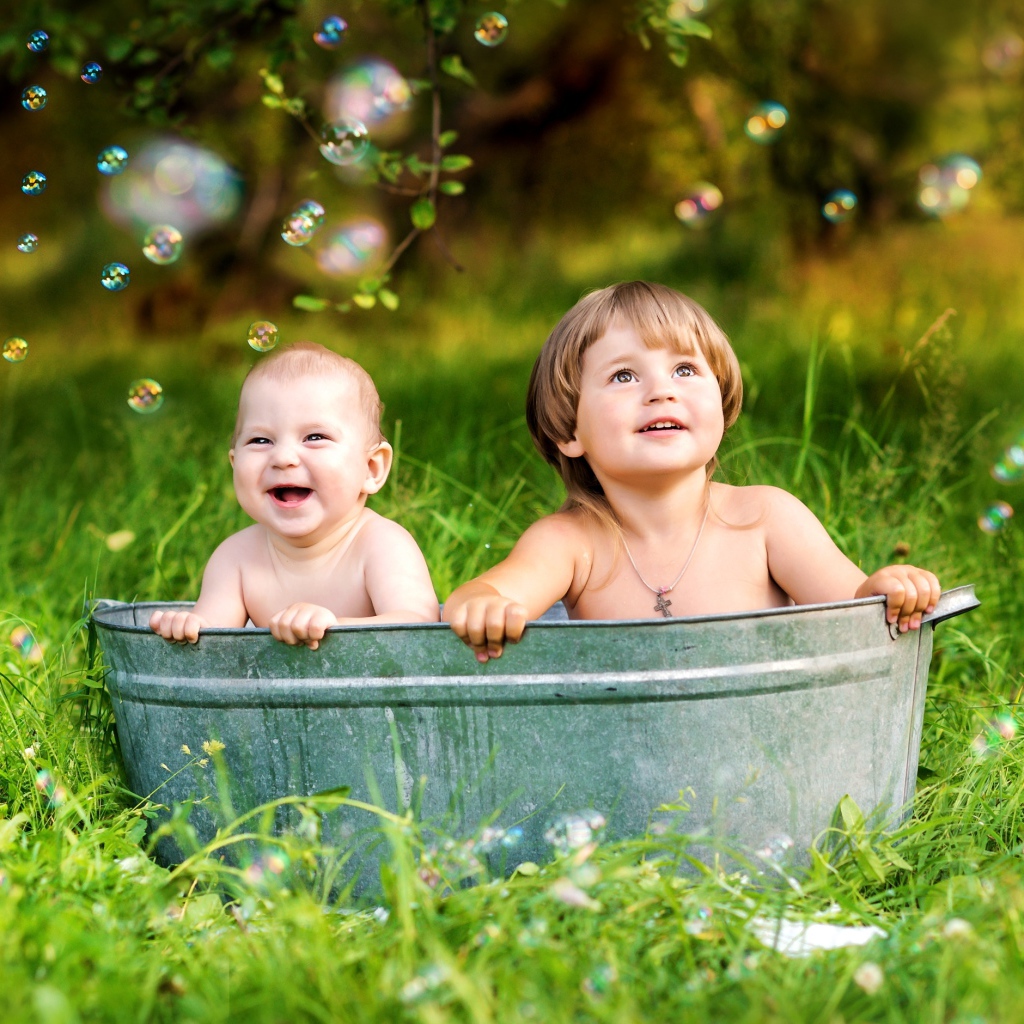 Два маленьких ребенка сидят в железном корыте на зеленой траве