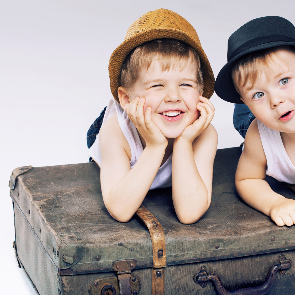 Два маленьких улыбающихся мальчика лежат на старом чемодане