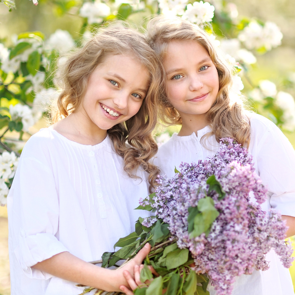 Две улыбающиеся девочки близняшки с букетом сирени