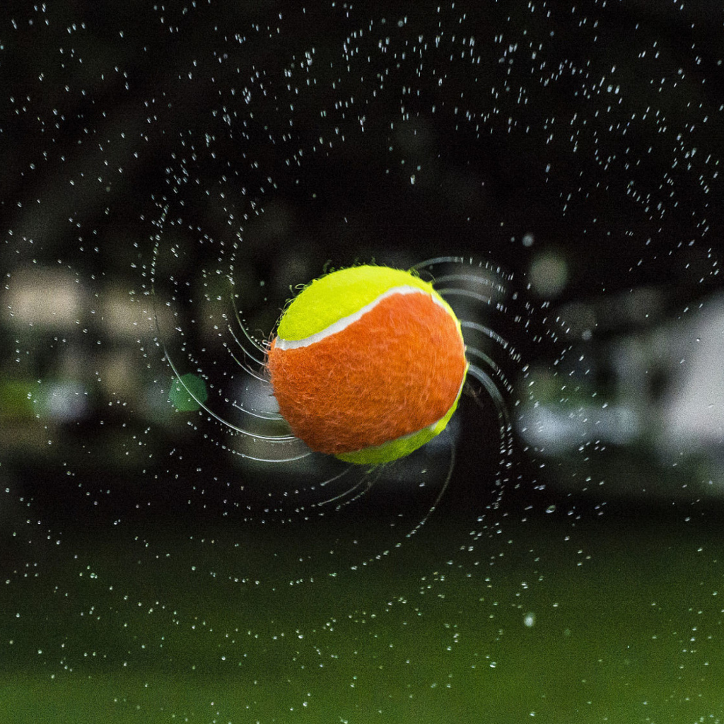 Теннисный мяч летит в каплях воды 