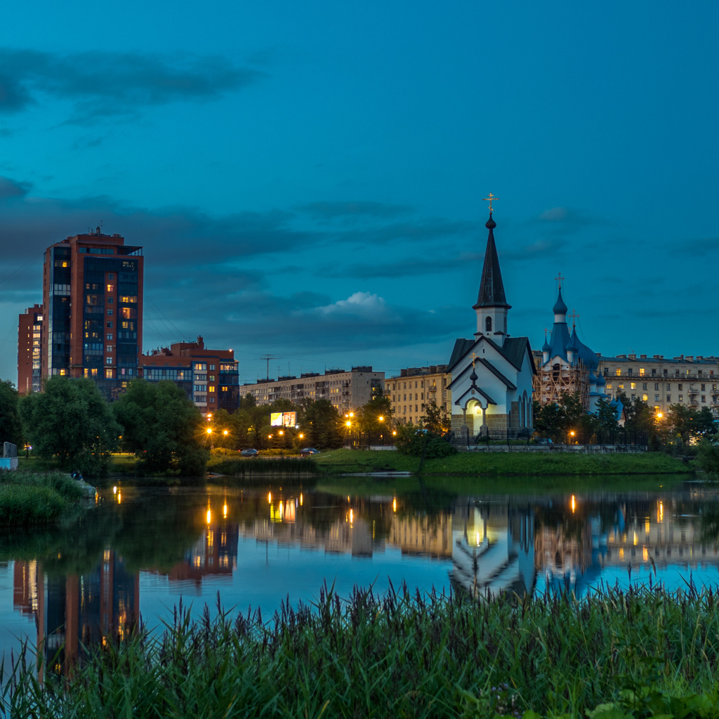 Вечерние огни маленькой церкви и домов отражаются в воде городского пруда, Санкт-Петербург. Россия