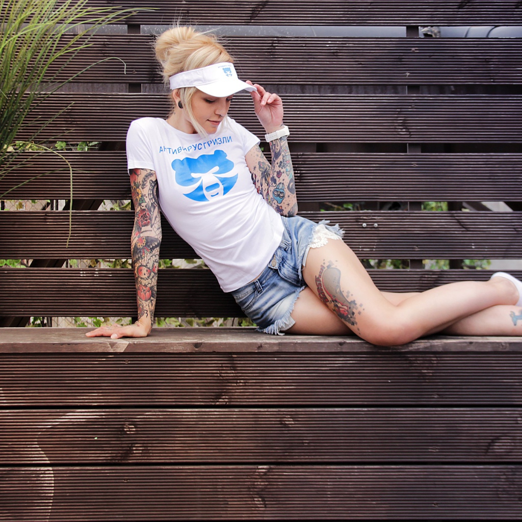 Спортивная девушка в татуировках лежит на деревянной лавке