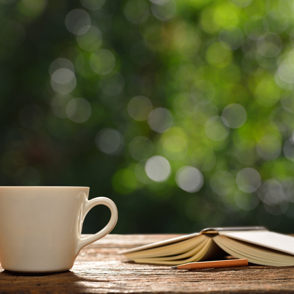 Белая чашка на столе с открытой книгой