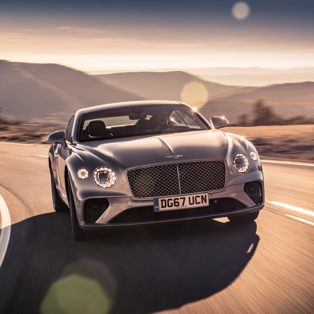 Серебристый автомобиль Bentley Continental GT 2018 года на трассе