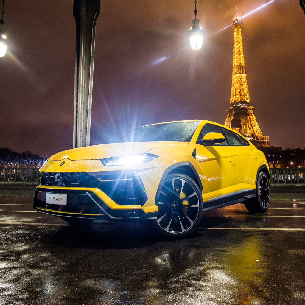 Желтый Lamborghini Urus, 2018 с включенными фарами на фоне Эйфелевой башни