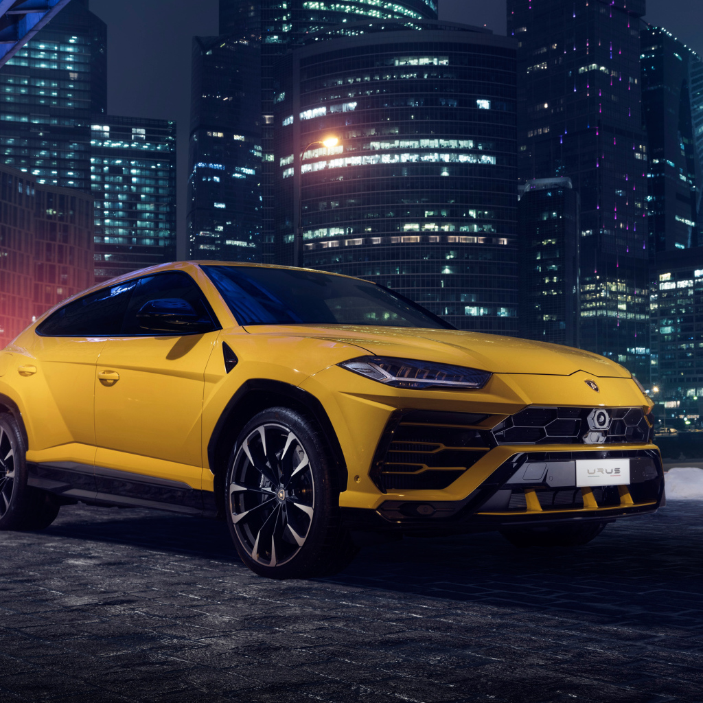 Желтый Lamborghini Urus на фоне ночных небоскребов