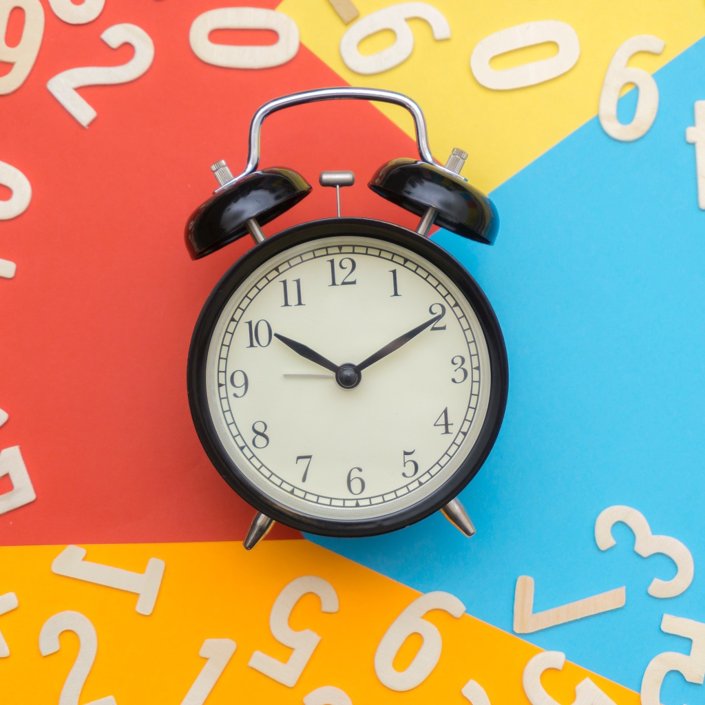 Будильник на разноцветном фоне с цифрами