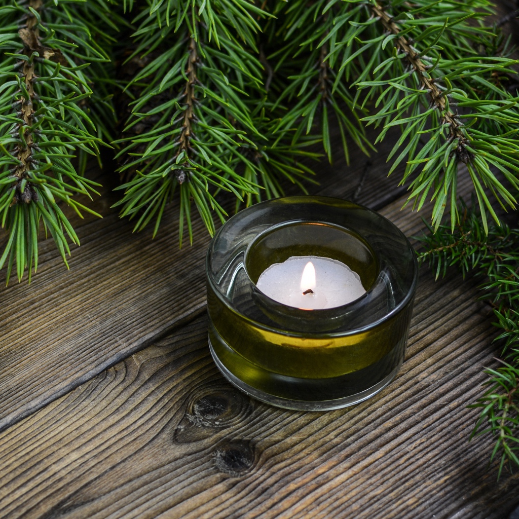 Зажженная свеча на столе с зеленой веткой ели