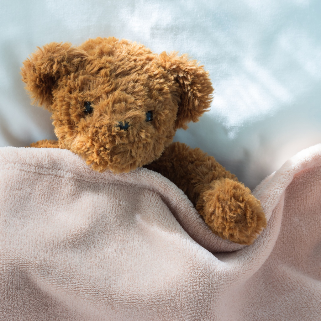 Плюшевый медведь в кровати под одеялом