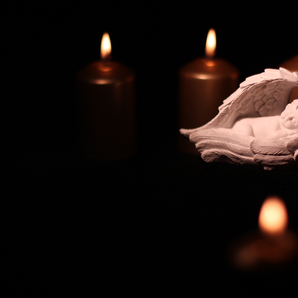 Фигурка ангела освещен горящими свечами на черном фоне