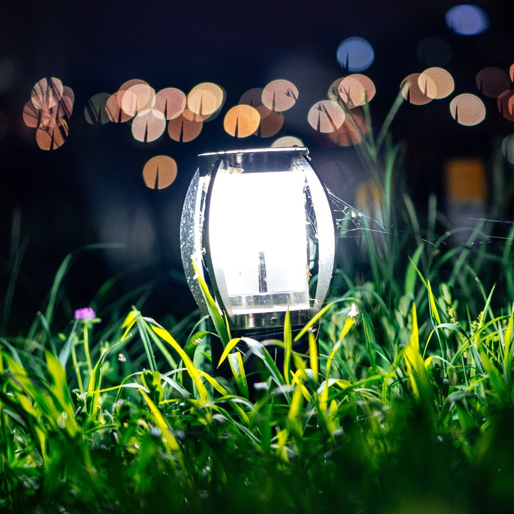 Включенный фонарь стоит в зеленой траве