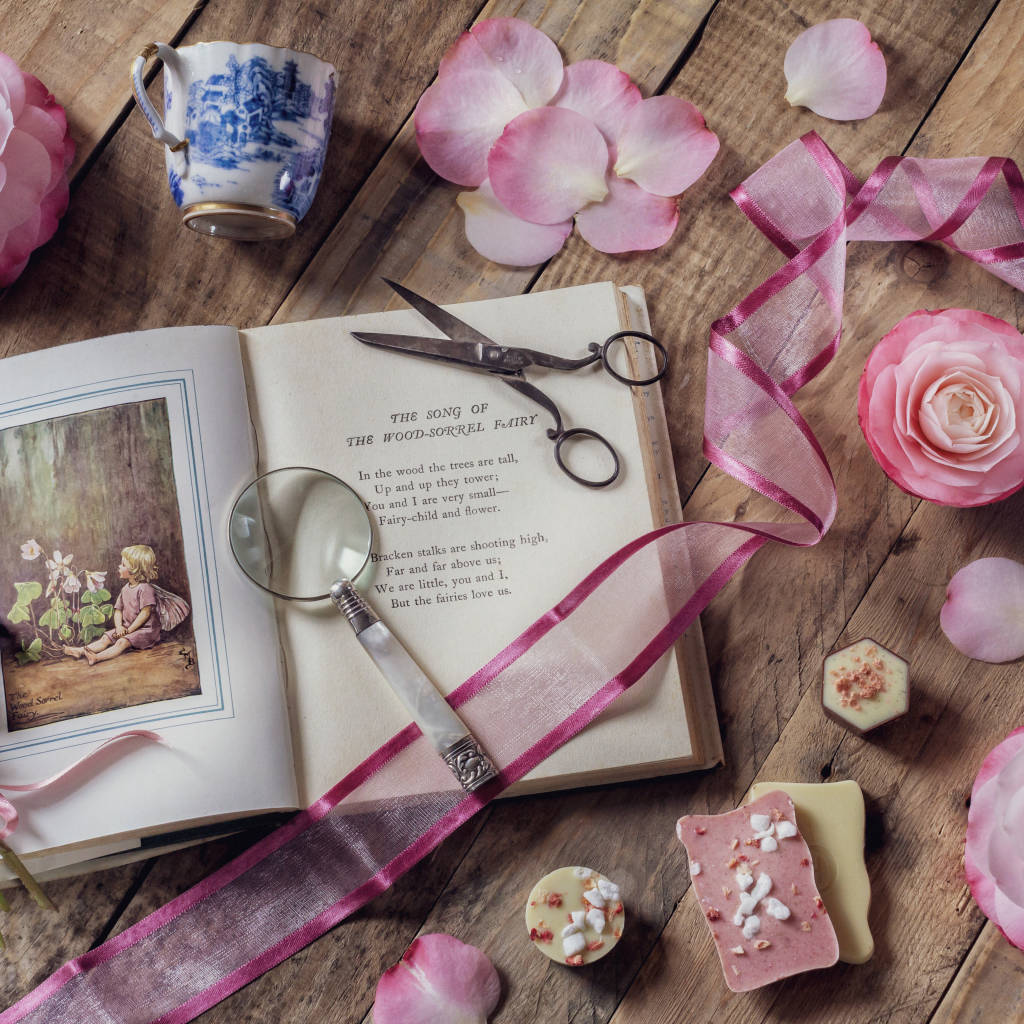 Старая книга на столе с увеличительным стеклом и искусственными цветами