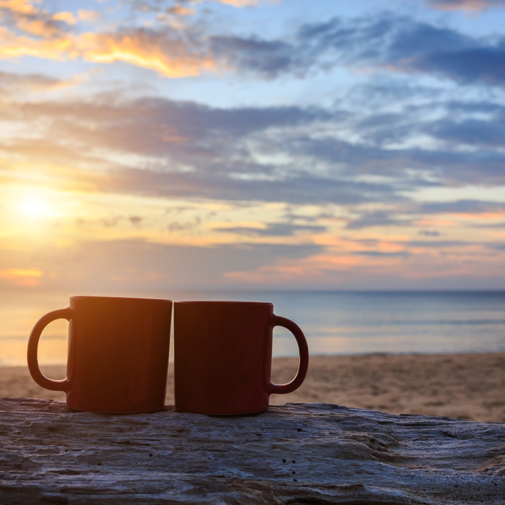 Две чашки стоят на песке на фоне рассвета 