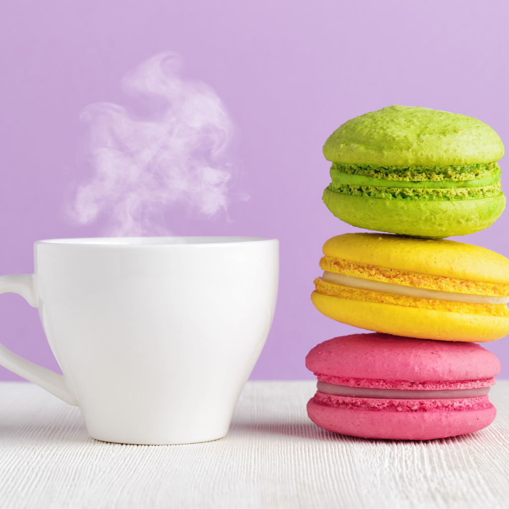 Разноцветный десерт макарун с чашкой горячего кофе на столе