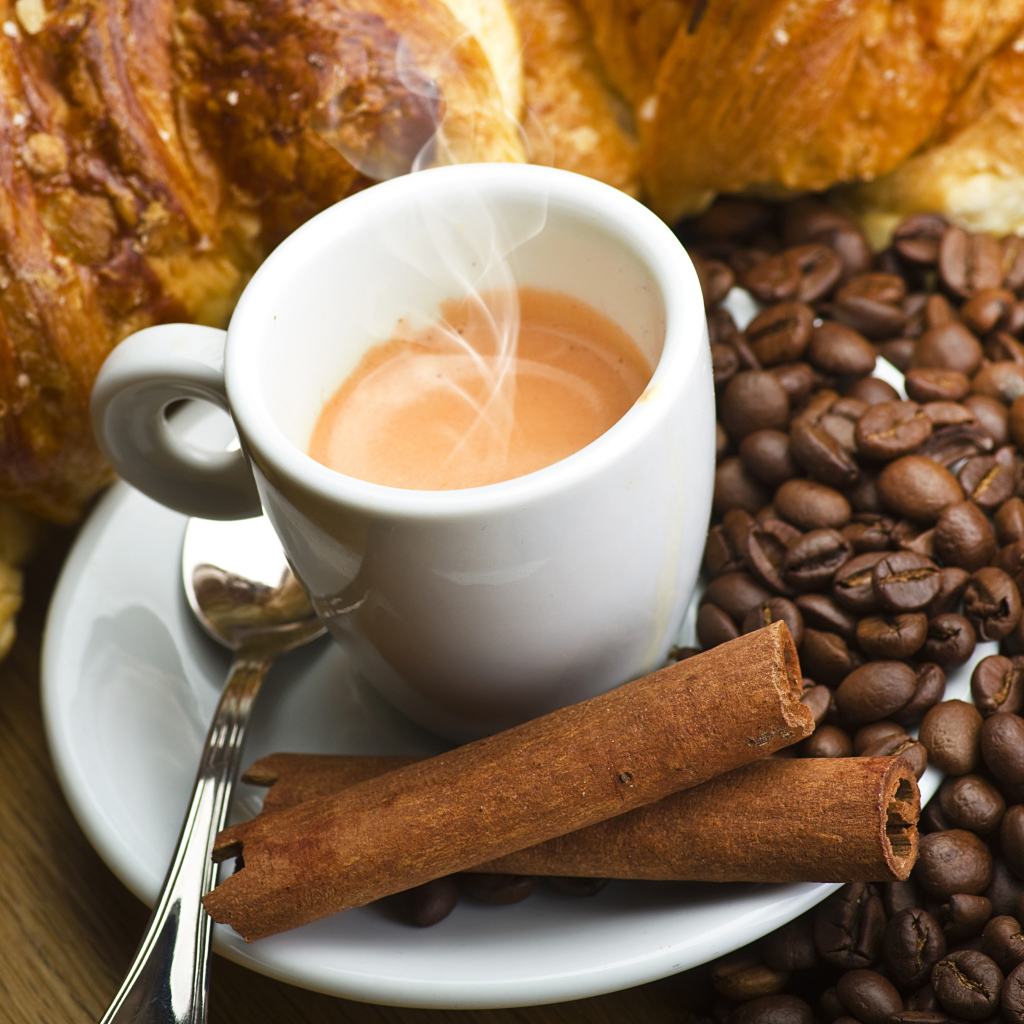 A cup of hot coffee on a table with cinnamon, coffee grains and pastries