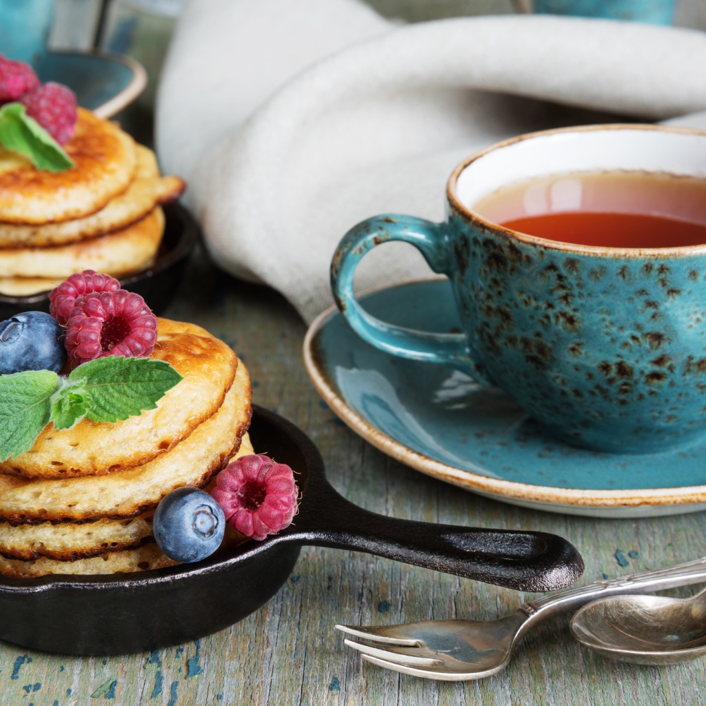 Чашка чаю с оладьями с ягодами на столе