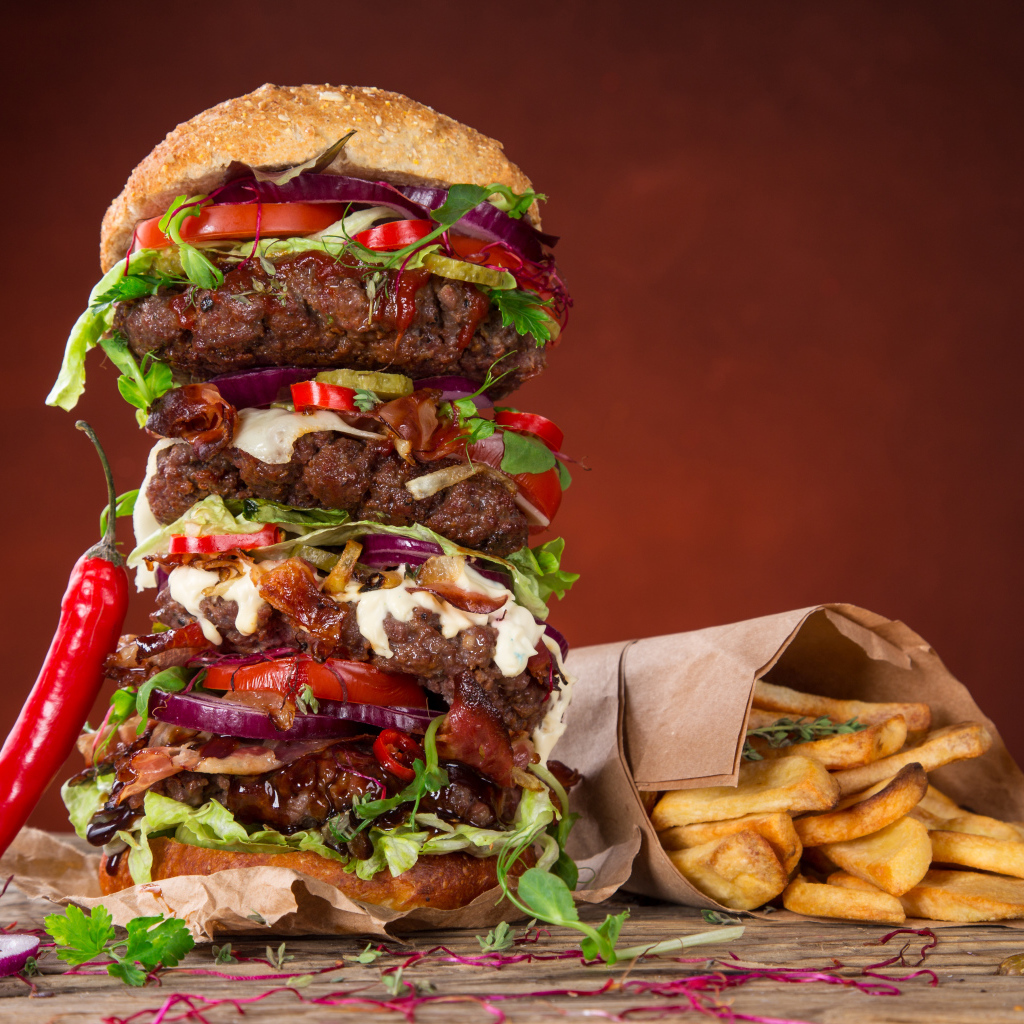 Огромный гамбургер на столе с картофелем фри и острым перцем